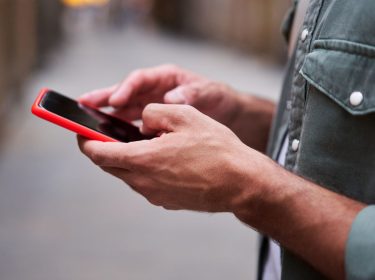 Zwei Hände halten ein Android-Handy mit roter Hülle.