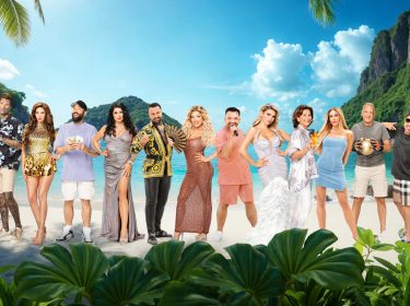 Auf dem Bild zur Reality-Show „Promis unter Palmen 2025“ stehen die Teilnehmer vor einer traumhaften Strandkulisse mit türkisblauem Wasser und tropischen Palmen. Zu sehen sind Lotto-Millionär Chico, Claudia Obert, Menowin Fröhlich, Janina Youssefian, Eike Immel, Iris Klein, Chris Manazidis, Kim Virginia, Cosimo Citiolo, Lisha Savage, Nikola Glumac und Melody Haase. Alle sind in glamourösen Outfits und präsentieren sich in selbstbewusser Pose.