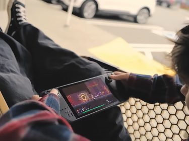 Ein junger Mann sitzt in einem Einkaufswagen und spielt ein Spiel auf einem Steam Deck