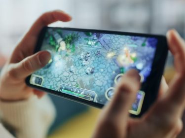 Zwei Hände halten ein Smartphone im Landscape-Modus, darauf läuft ein Mobile Game.