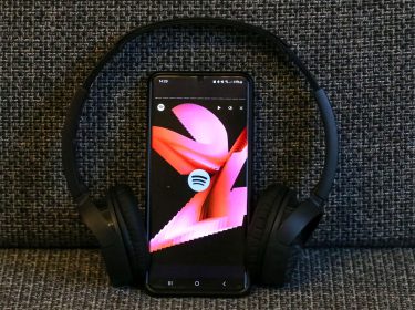Ein Smartphone mit dem Spotify Logo und der Animation von Spotify Wrapped sowie ein Kopfhörer sind zu sehen.