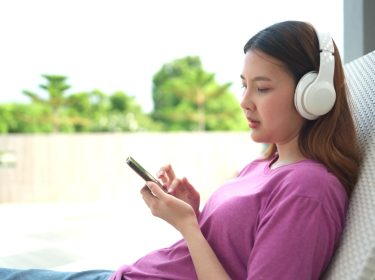 Frau im lila Shirt mit Kopfhörern schaut auf ihr Smartphone