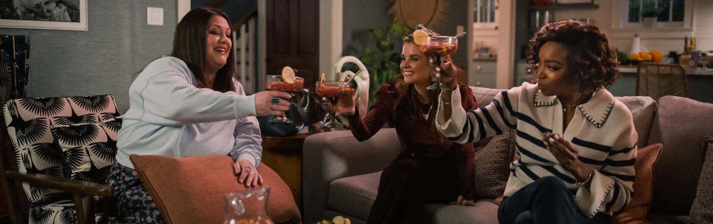 Drei Frauen stoßen in einem Wohnzimmer mit Getränken an.