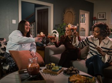 Drei Frauen stoßen in einem Wohnzimmer mit Getränken an.