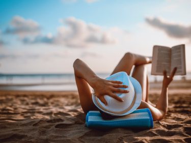 Eine Frau liest am Strand liegend ein Buch.