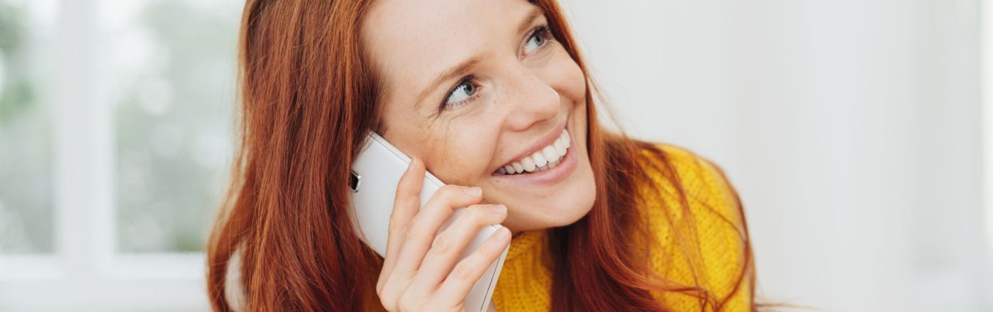 Eine lächelnde rothaarige Frau telefoniert mit dem Smartphone