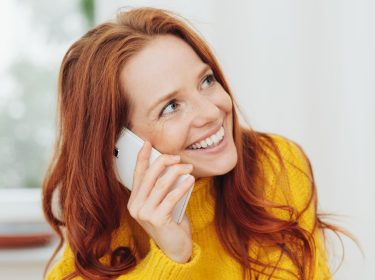 Eine lächelnde rothaarige Frau telefoniert mit dem Smartphone