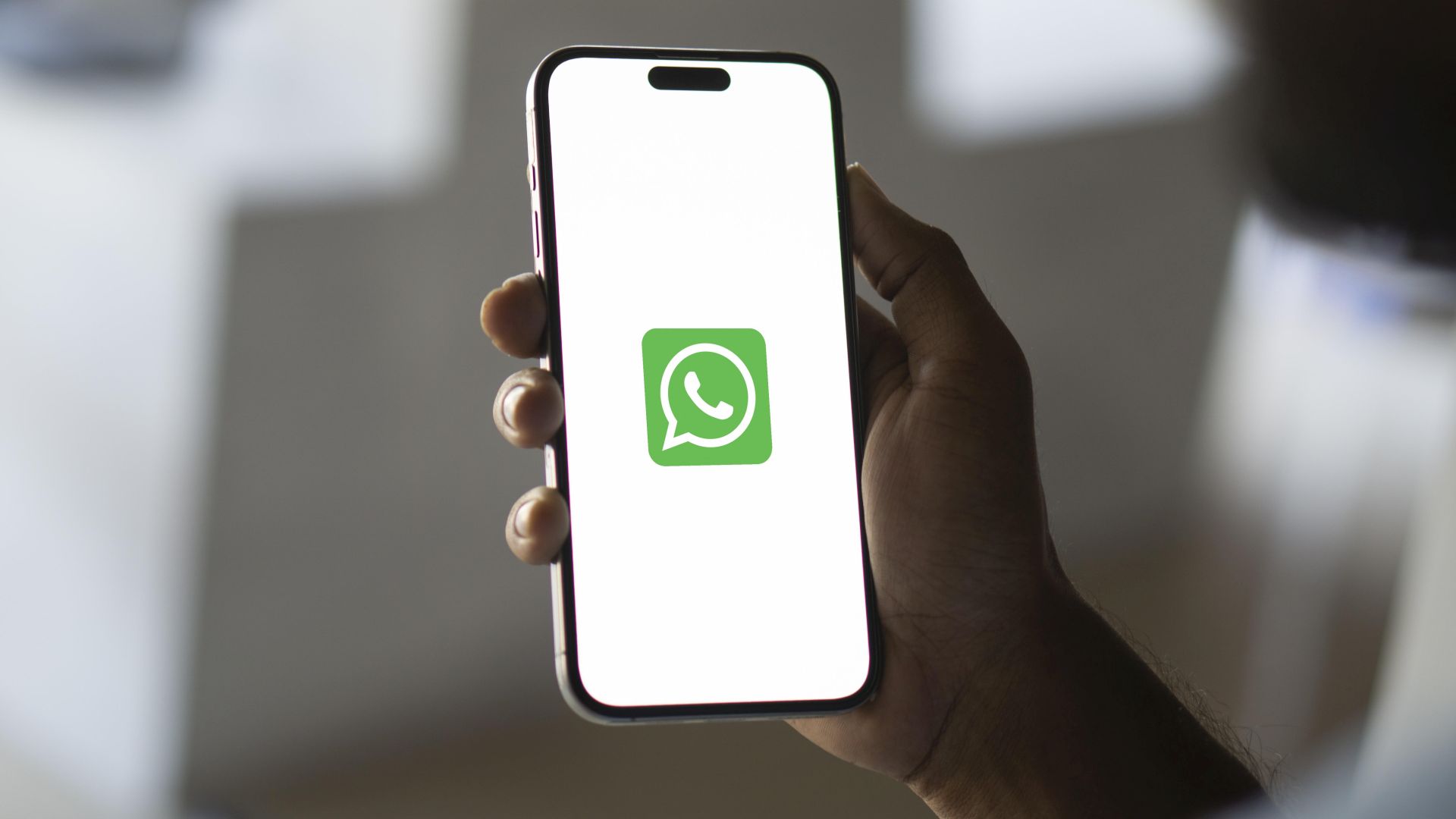 Hand hält ein iPhone hoch, auf dem das WhatsApp-Logo auf weißem Hintergrund abgebildet ist.