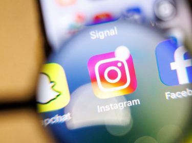 Die Instagram-App ist durch eine Lupe auf einem Smartphone zu sehen.