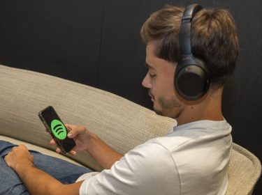 Mann mit Kopfhörern sitzt auf Couch und schaut auf sein Smartphone