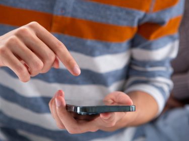 Ein Mann hält ein iPhone in der Hand und bedient es mit dem Zeigefinger.