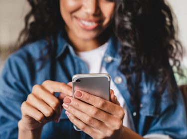 Eine junge Frau hält ein Smartphone in der Hand und lächelt
