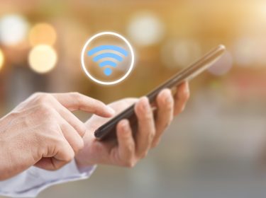 Nahaufnahme einer Hand, die ein Smartphone bedient. Darüber schwebt ein WLAN-Symol.