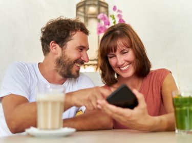 Ein Mann und eine Frau schauen auf ein Smartphone und lachen dabei.