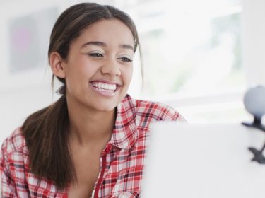 Eine junge Frau schaut in die Webcam, die an ihrem Laptop angebracht ist.