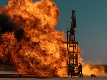 Arbeiter stehen um eine Ölbohrung herum, die Feuer gefangen hat.