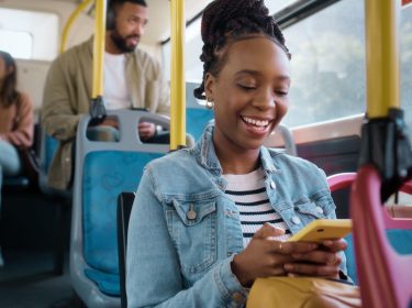 Eine junge Frau schaut im Bus auf ihr Smartphone und lächelt.