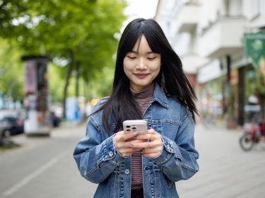 Eine junge Frau nutzt ihr Handy, während sie auf einem Bürgersteig steht