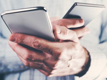 Ein Mann hält in jeder Hand ein Smartphone.