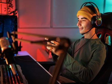Ein junger Mann sitzt auf einem PC-Stuhl, hält einen Controller in der Hand und spielt am Computer.