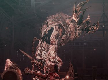 In dem Bild für The First Berserker: Khazan Tipps ist ein riesiges, kettenbewehrtes Monster mit zotteligem Fell und knochigem Geweih in einer düsteren Arena zu sehen.