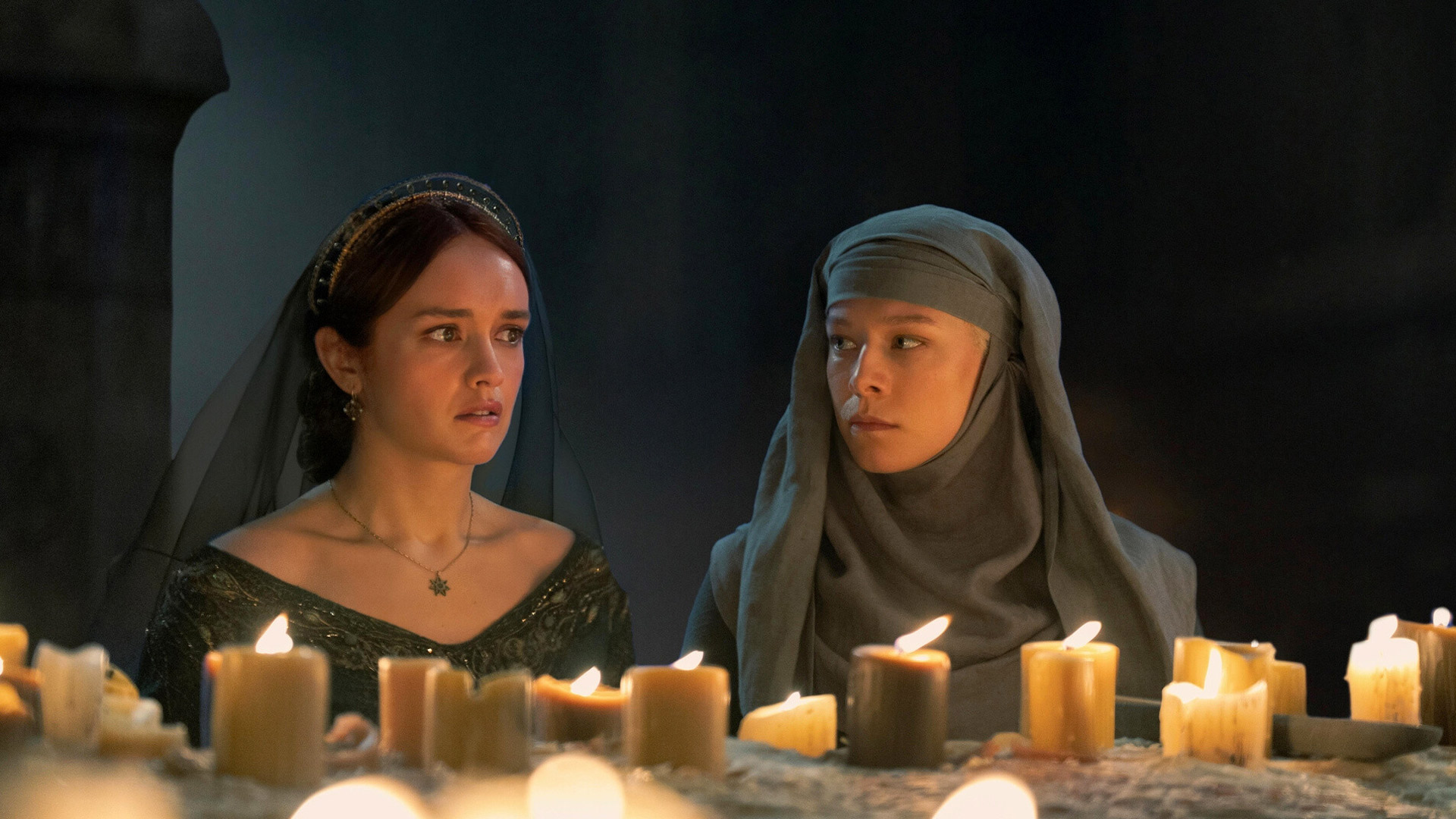 In dieser Szene aus House of the Dragon Staffel 2 sitzen Alicent Hohenturm, gespielt von Olivia Cooke, und Rhaenyra Targaryen, dargestellt von Emma D’Arcy, schweigend vor einem Altar mit brennenden Kerzen. Beide wirken angespannt und nachdenklich – ein stiller, aber intensiver Moment, der die Spannung für House of the Dragon Staffel 3 weiter aufbaut.