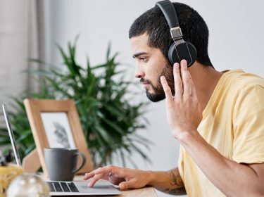 Ein Mann trägt Kopfhörer und arbeitet am Laptop