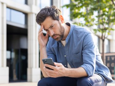 Ein Mann schaut nachdenklich auf das Display seines Smartphones.