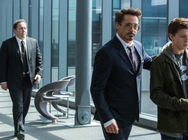 In dieser Szene aus einem der Filme von Robert Downey Jr. steht Tony Stark, gespielt von Robert Downey Jr., links im Bild und blickt ernst auf Peter Parker, dargestellt von Tom Holland. Die beiden stehen sich gegenüber in einem Moment voller Spannung und Bedeutung. Die Lichtstimmung ist dramatisch, mit urbanem Hintergrund und deutlichen Kontrasten zwischen den Figuren.