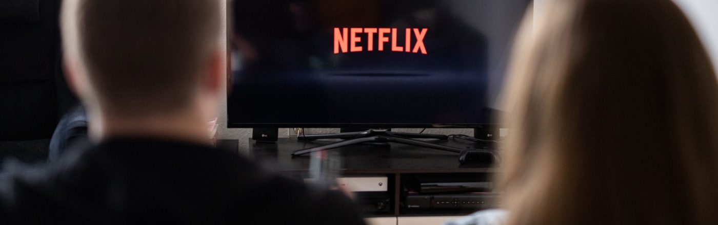 Junges Paar schaut auf einen Fernseher, auf dem das Netflix-Logo abgebildet ist