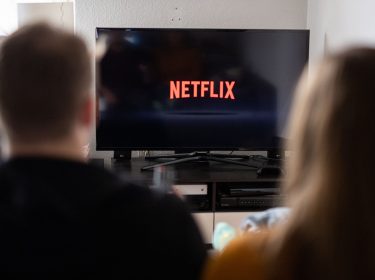 Junges Paar schaut auf einen Fernseher, auf dem das Netflix-Logo abgebildet ist