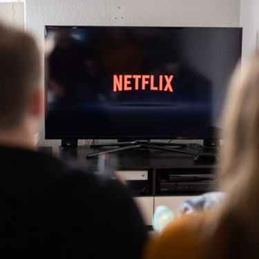 Junges Paar schaut auf einen Fernseher, auf dem das Netflix-Logo abgebildet ist