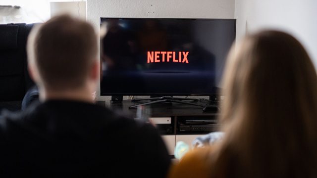 Junges Paar schaut auf einen Fernseher, auf dem das Netflix-Logo abgebildet ist