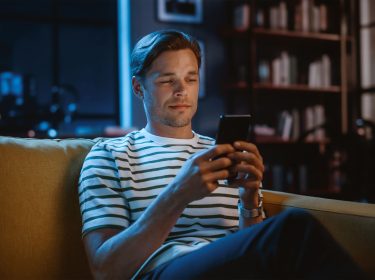 Ein Mann sitzt auf einem Sofa und hält ein Smartphone in der Hand.