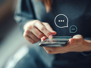 Eine Frau hält ein Smartphone in der Hand. Über dem Smartphone sind zwei Sprechblasen als Nachrichtensymbol abgebildet.