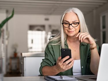 Eine Frau sitzt an einem Tisch und hält ein Smartphone in der Hand.