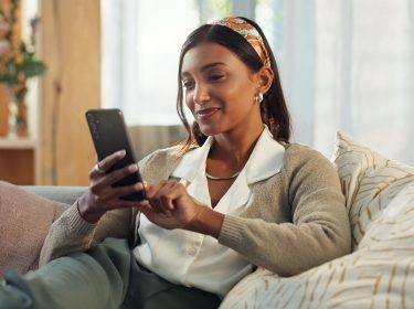 Frau sitzt auf Sofa und tippt auf ihr Android-Smartphone.