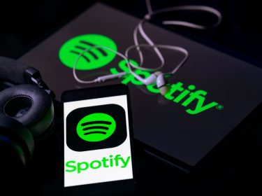 Das Spotify-Logo ist auf einem Smartphone und einem Tablet zu sehen, die neben einem Kopfhörer liegen.