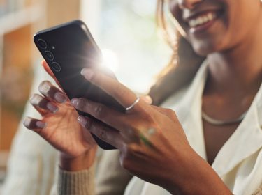 Frau schaut lächelnd auf ihr Samsung-Handy.