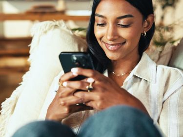 Frau schaut lächelnd auf ihr Smartphone.