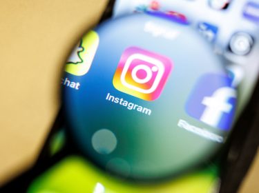 Die Instagram-App ist durch eine Lupe auf einem Smartphone zu sehen.