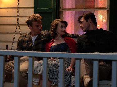 Im Bild zur On Swift Horses-Kritik sitzen Lee (Will Poulter), Muriel (Daisy Edgar-Jones) und Julius (Jacob Elordi) eng nebeneinander auf einer Veranda-Schaukel. Die Stimmung wirkt gespannt und emotional aufgeladen. Muriel sitzt zwischen den beiden Männern, schaut Julius direkt an, während Lee sie beschützend umfasst. Im Hintergrund leuchtet warmes Licht durch ein Fenster und verstärkt die intime Atmosphäre der Szene.