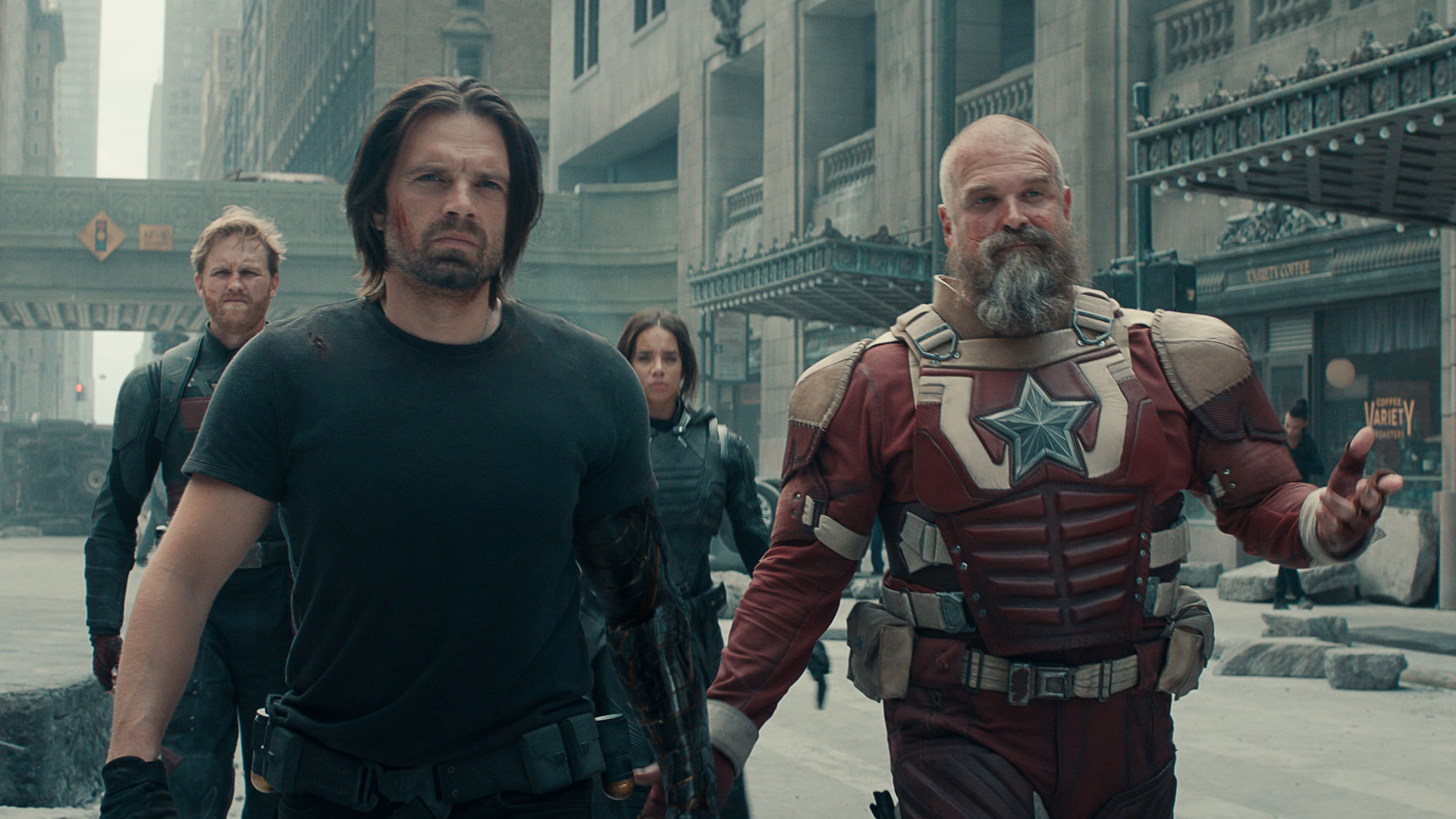 Auf dem Bild zur Thunderbolts* Kritik marschieren John Walker (Wyatt Russell), Bucky Barnes (Sebastian Stan), Ghost (Hannah John-Kamen) und Red Guardian (David Harbour) entschlossen durch eine zerstörte Stadt. Im Vordergrund sieht man Bucky mit grimmigem Blick und Red Guardian in rot-weißer Rüstung, der mit einer Geste spricht. Die Szene wirkt angespannt, dynamisch und zeigt das Team in Aktion.