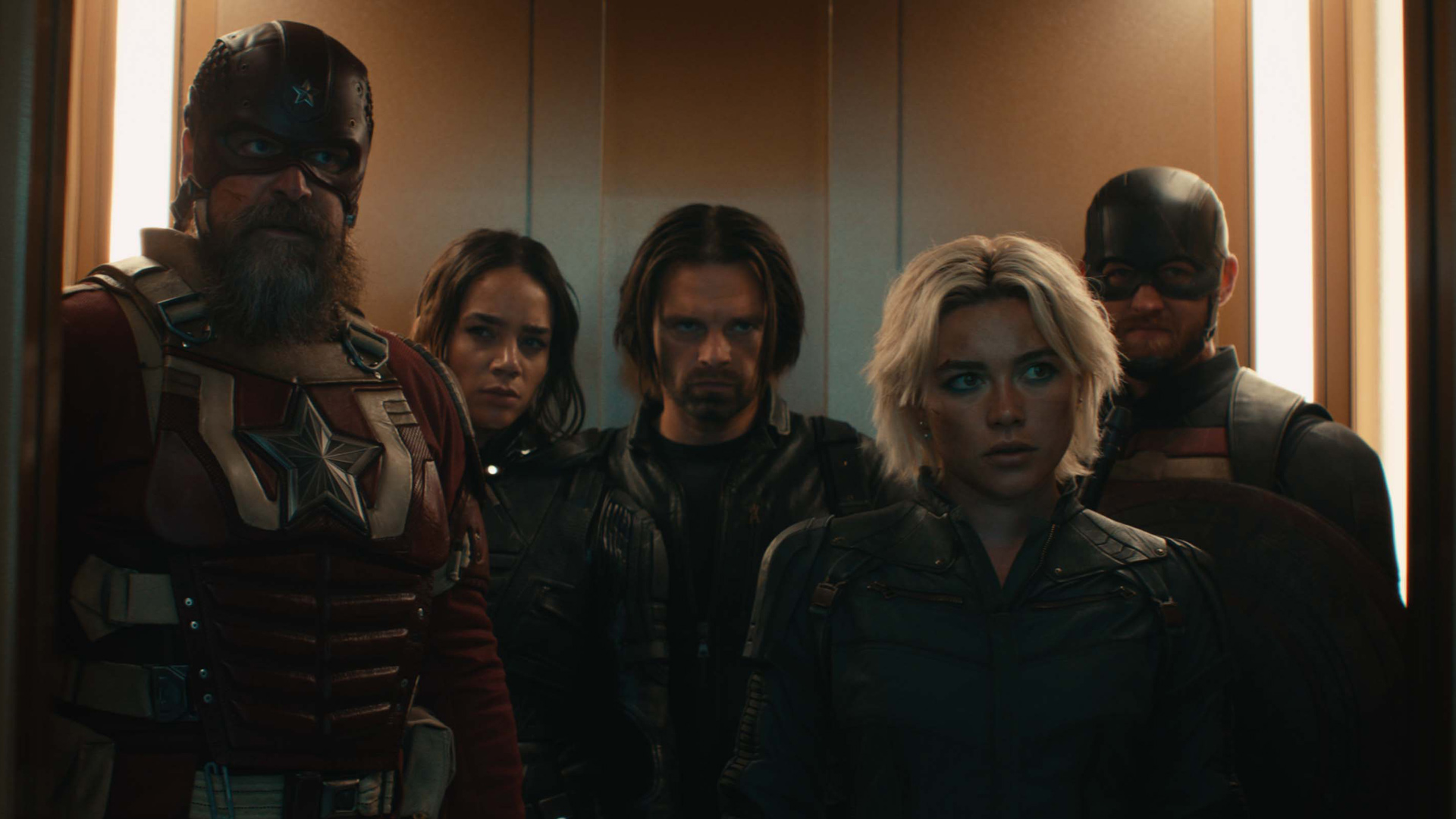 Auf dem Bild zur Thunderbolts* Kritik stehen Red Guardian (David Harbour), Ghost (Hannah John-Kamen), Bucky Barnes (Sebastian Stan), Yelena Belova (Florence Pugh) und John Walker (Wyatt Russell) in einem engen Aufzug nebeneinander. Alle Figuren blicken ernst und konzentriert, die Stimmung ist angespannt. Die Szene ist düster ausgeleuchtet und vermittelt den Moment vor einem entscheidenden Einsatz.