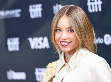 Auf dem Bild in dem Artikel zur möglichen Split Fiction-Verfilmung ist Schauspielerin Sydney Sweeney zu sehen. Sie steht lächelnd vor einer Pressewand und trägt ein elegantes, cremefarbenes Outfit mit floralen Details. Das Bild vermittelt eine positive, glamouröse Stimmung.