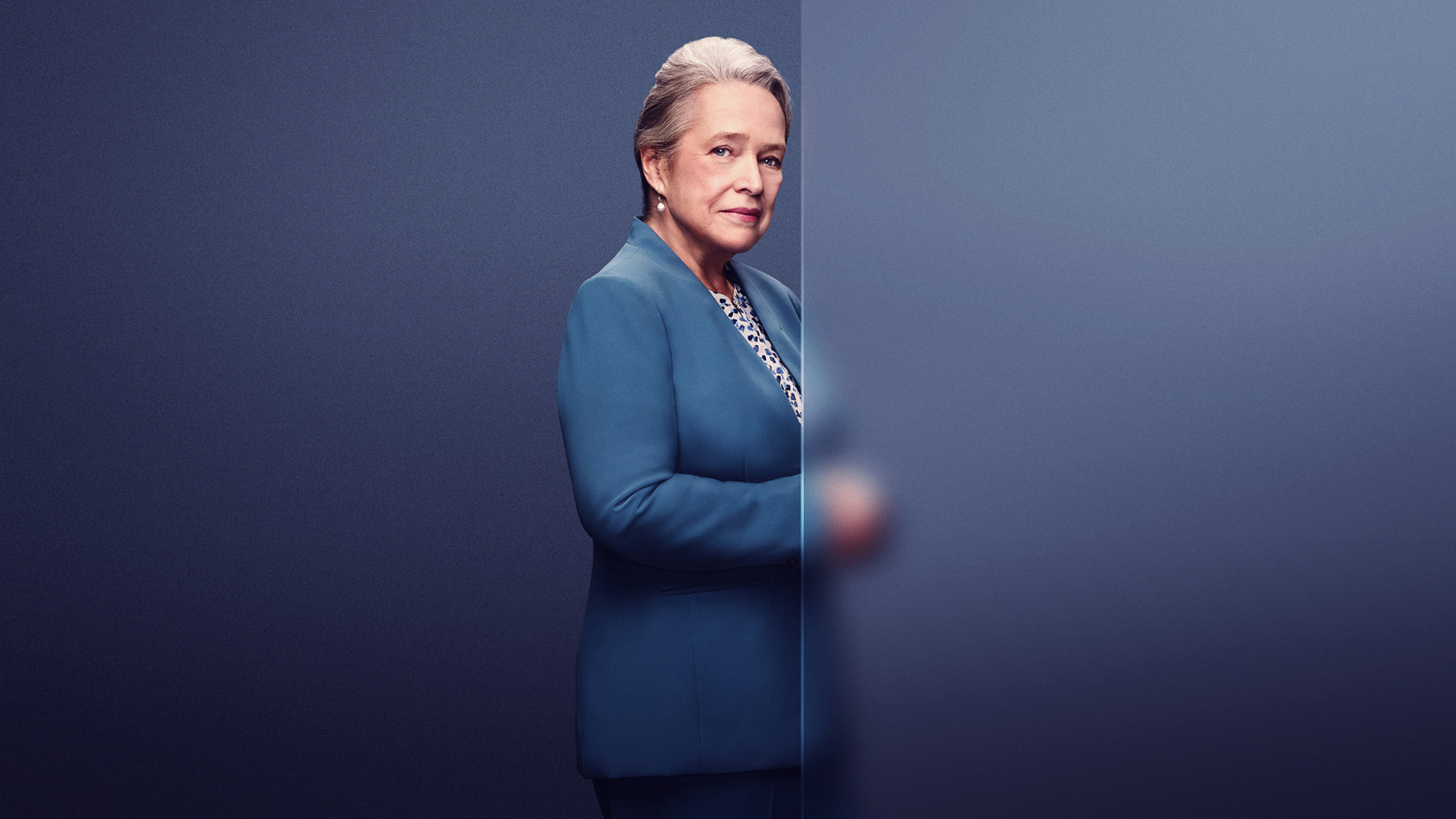 Das Bild zu den GigaTV-Highlights im Mai zeigt eine Szene aus der Serie „Matlock“. Im Zentrum steht die Hauptfigur Madeline „Maddy“ Matlock, gespielt von Kathy Bates, in einem eleganten blauen Anzug. Sie blickt mit ruhiger Entschlossenheit zur Kamera, während sie hinter einer halbtransparenten Wand hervorschaut. Das Setting wirkt nüchtern und seriös – passend zum juristischen Kontext der Serie.