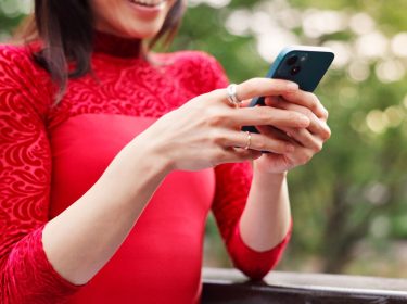 Junge Frau in rotem Shirt schaut lächelnd auf ihr iPhone.