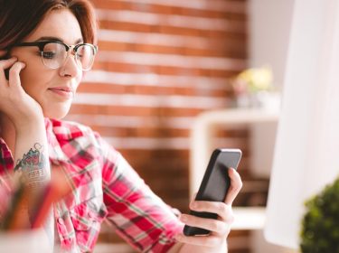 Eine rothaarige Frau schaut auf ihre Smartphone.