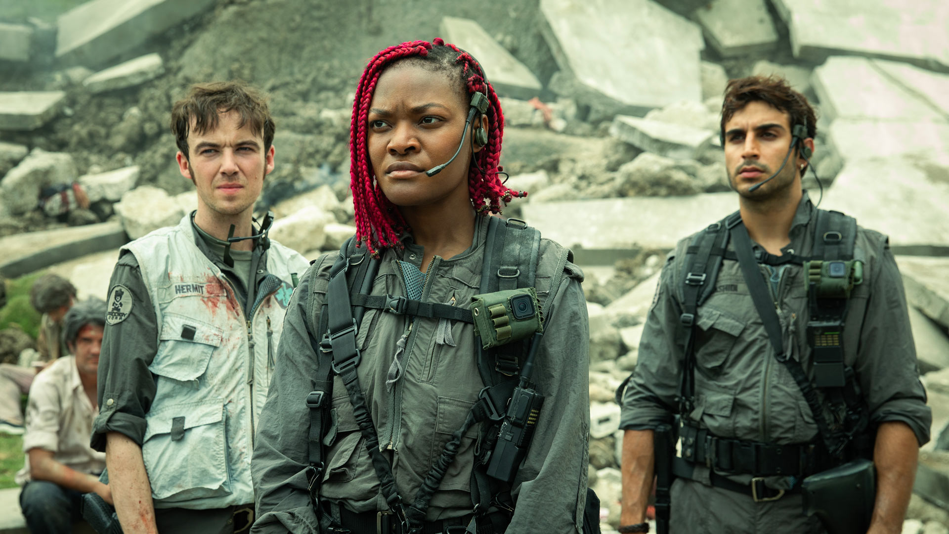 In der Alien: Earth Serie stehen Hermit, Siberian und Rashidi – gespielt von Alex Lawther, Diêm Camille und Moe Bar-El – inmitten einer zerstörten Betonlandschaft. Alle drei tragen taktische Kampfanzüge mit Headsets und schauen konzentriert in unterschiedliche Richtungen. 