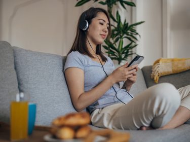 Eine Frau sitzt auf dem Sofa und hört über Kopfhörer Musik vom Android-Smartphone.